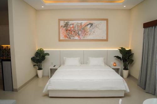 a bedroom with a white bed and a painting on the wall at Gelis Gede Cottages in Uluwatu