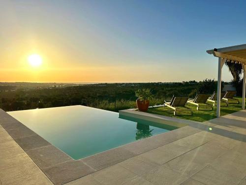 a swimming pool with chairs and a sunset in the background at Casa BelaVista - Fuzeta in Moncarapacho