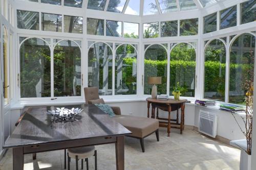 une véranda avec une table, des chaises et des fenêtres dans l'établissement Maison au calme près de Versailles, à Louveciennes