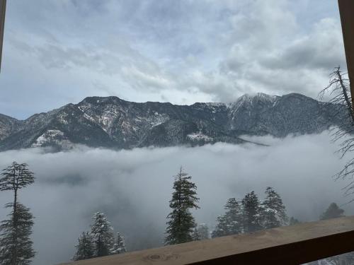 a view of a mountain range with clouds and trees at Hunting Wood Kathkuni Attic Cottage in Mandi
