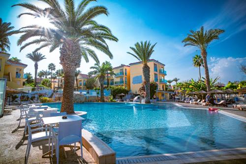 a pool at a resort with palm trees and chairs at Malama Beach Holiday Village in Protaras