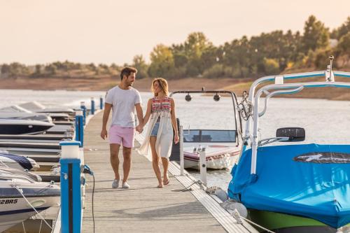 a man and woman walking on a dock next to boats at AP Lago Montargil - Conference & SPA in Montargil