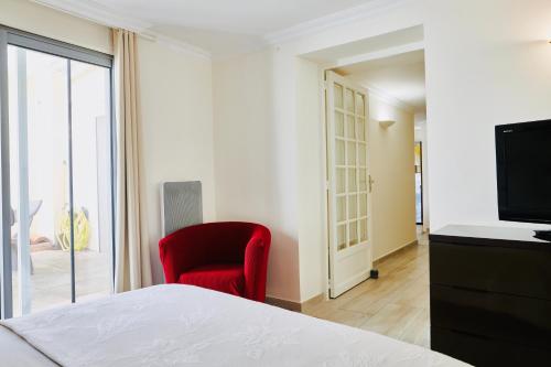 a bedroom with a red chair and a television at Le Cocon de ville sètois, Clim, patio et garage pour véhicule type golf, Linge de lit et serviettes inclus in Sète