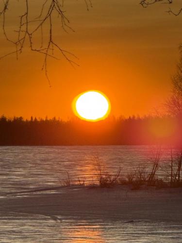 a sunset over a body of water with the sun setting at Sampo Chalet with Hot Tub in Ranua