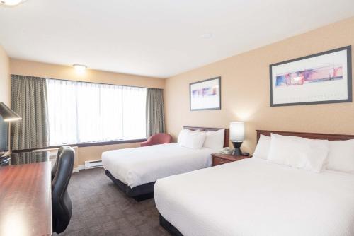 a hotel room with two beds and a desk at Sandman Hotel Castlegar in Castlegar