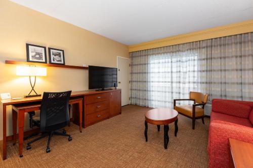 a hotel room with a desk and a couch and a television at Courtyard Toledo Airport Holland in Holland