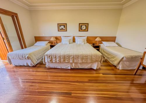 two beds in a hotel room with wooden floors at Pousada Victoria Villa By Nacional Inn - A 800 metros da Vila Capivari in Campos do Jordão