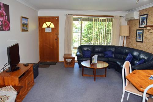 a living room with a black leather couch and a table at Sunny Nook - Bring your own linen. in South West Rocks