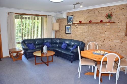 a living room with a black leather couch and a table at Sunny Nook - Bring your own linen. in South West Rocks