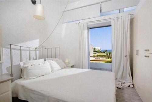 a white bedroom with a bed and a large window at Agistri House Pefkohori in Pefkochori