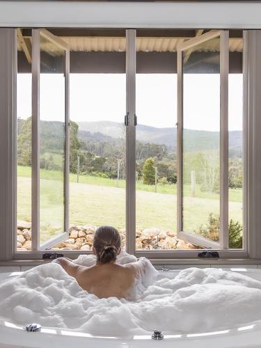 a man laying in a bath tub in front of a window at Fellcroft Farmstay in Cobaw