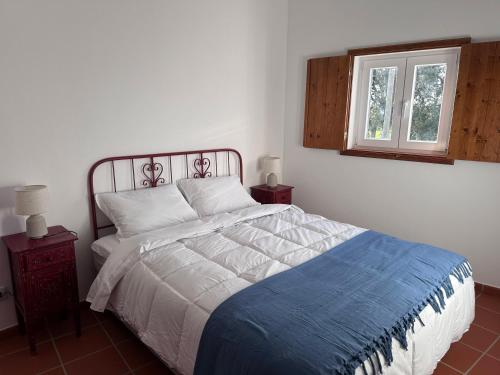 a bedroom with a bed with a blue blanket and a window at Herdade do Vidigal in Montemor-o-Novo