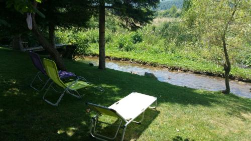 two chairs and a table in the grass next to a river at Rustic Inn River 2 in Plitvička Jezera