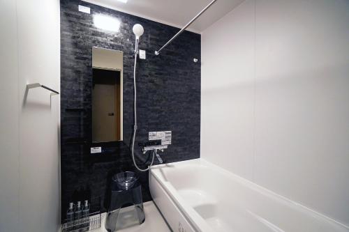 a bathroom with a white tub and a black tile wall at Purpure Furano in Kami-furano