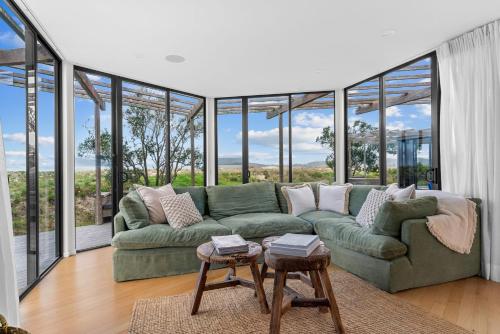 a living room with a green couch and large windows at Wavefront Escape - Omaha Holiday Home in Warkworth