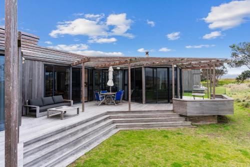 a house with a deck with a table and chairs at Wavefront Escape - Omaha Holiday Home in Warkworth