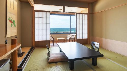 a room with a table and chairs with a view of the ocean at 竹屋ホテル in Tsuruoka