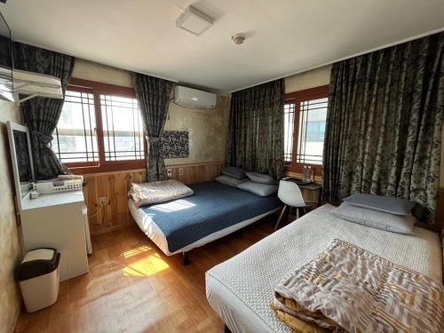 a bedroom with two beds and a desk and windows at Gudeok Guesthouse in Seogwipo