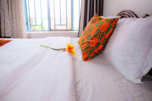 a white bed with an orange pillow and a flower on it at Kivu Greenstars Apartment in Gisenyi