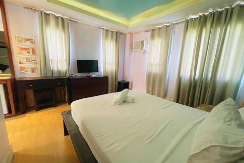 a bedroom with a white bed with curtains and a television at Here Innstead Boracay in Boracay