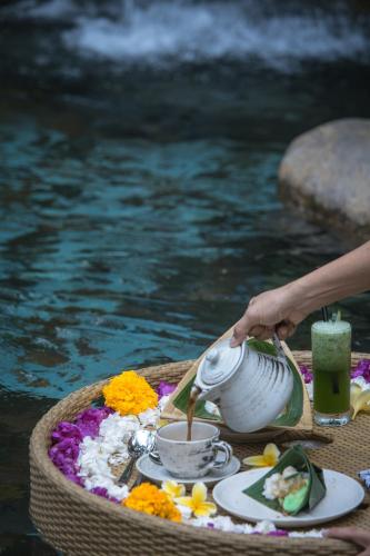 a person is pouring a drink from a pot on a table by the water at Pramana Giri Kusuma in Payangan