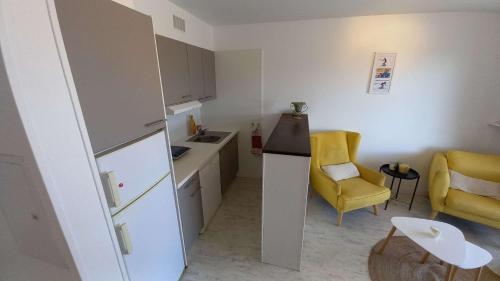 Elle comprend une petite cuisine équipée d'un réfrigérateur blanc et d'une chaise jaune. dans l'établissement Appartement 2 pièces climatisé 3 couchages, Belle Terrasse VUE MER à Portiragnes plage LXBFM9, à Portiragnes