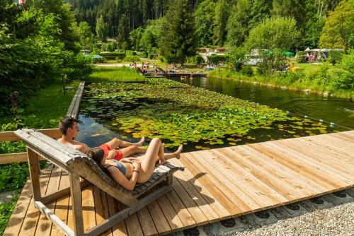 two people laying on a bench next to a pond at Alpenferienpark Reisach in Reisach
