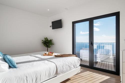 a white bedroom with a bed and a balcony at VIRA by KAAMAH in Estreito de Câmara de Lobos