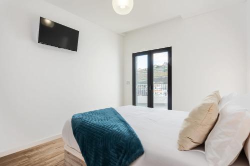 a white bedroom with a bed and a tv on the wall at VIRA by KAAMAH in Estreito de Câmara de Lobos
