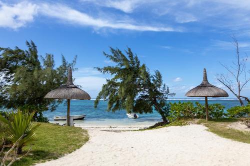 a beach with two umbrellas and a bench and the ocean at Tropical beachfront apartment in Belle Mare