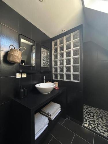 une salle de bain noire avec un lavabo et un miroir dans l'établissement Maison de village sud Touraine avec piscine proche Chinon Azay, à Tavant