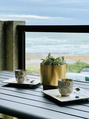 une table avec deux tasses et une plante en pot devant une fenêtre dans l'établissement Mon rêve mer, à Les Sables-dʼOlonne