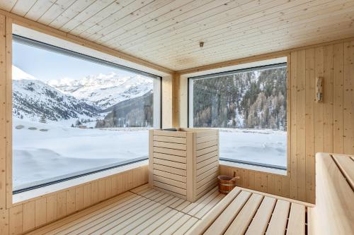 a sauna with a large window and snowy mountains at Hotel Alpenjuwel in Melago