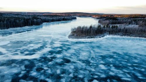 an aerial view of a frozen river with trees at Silver Birch Resort Lapland in Rovaniemi