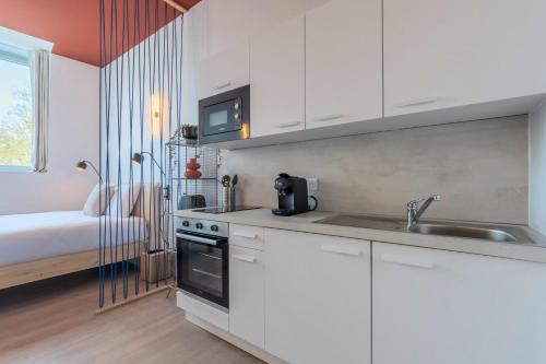 une cuisine avec des armoires blanches et un évier et un lit dans l'établissement Studio équipé côté rue, parking gratuit, à Villeneuve d'Ascq