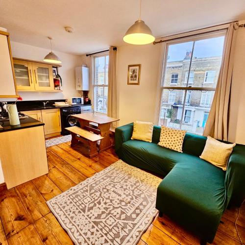 a living room with a green couch and a kitchen at Lovely 1 Bed Apartment 2 min to Station in London