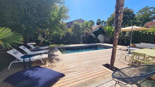 une terrasse en bois avec une piscine, des chaises et un parasol dans l'établissement Magnifique Villa 500 M Ocean 5 min du lac Hossegor, à Capbreton