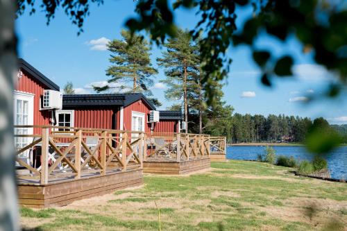 a red house with a wooden fence next to a lake at First Camp Orsa - Dalarna in Orsa
