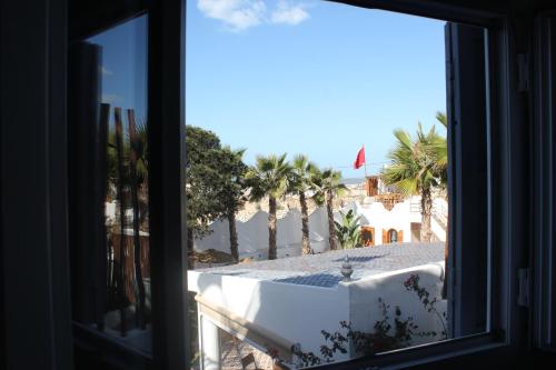 a window with a view of the beach and palm trees at La Maison des Vagues in Sidi Kaouki