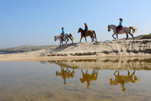a group of people riding horses on the beach at Herdade Do Pessegueiro in Porto Covo