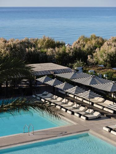 a pool with chairs and umbrellas next to the ocean at Doryssa Seaside Resort in Pythagoreio