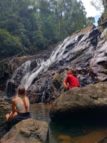 three people sitting on rocks in front of a waterfall at Rainforest cabin in Deniyaya