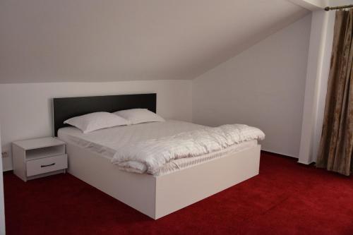 a bedroom with a white bed and a red carpet at Pensiunea Maria Mihăești in Mihăeşti