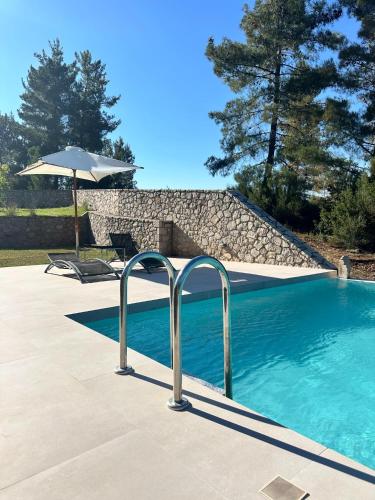 a swimming pool with an umbrella next to a stone wall at Alti Parnassos Residences in Amfiklia