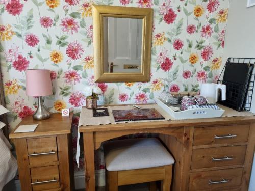 a desk with a mirror on a wall with flowers at Montfort Cottage Guest House in Windermere