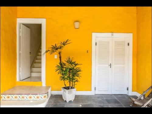 a yellow wall with two white doors and a plant at Vila Giulia in Maresias