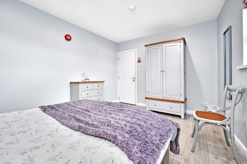 a white bedroom with a purple bed and a chair at Stylish apartment close to Causeway Coast & Glens in Portglenone