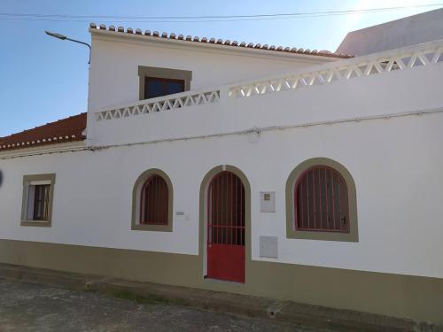 a white building with red doors and windows at Casa da Alzira T2 in Vila Nova de Milfontes