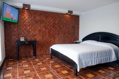 a bedroom with a bed and a tv on a brick wall at Hostería El Prado in Ibarra