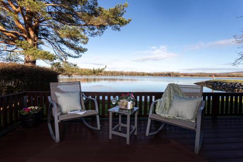 two chairs and a table on a deck next to a lake at Sandmartin Lodge a lakeshore haven Pine Lake Resort in Carnforth